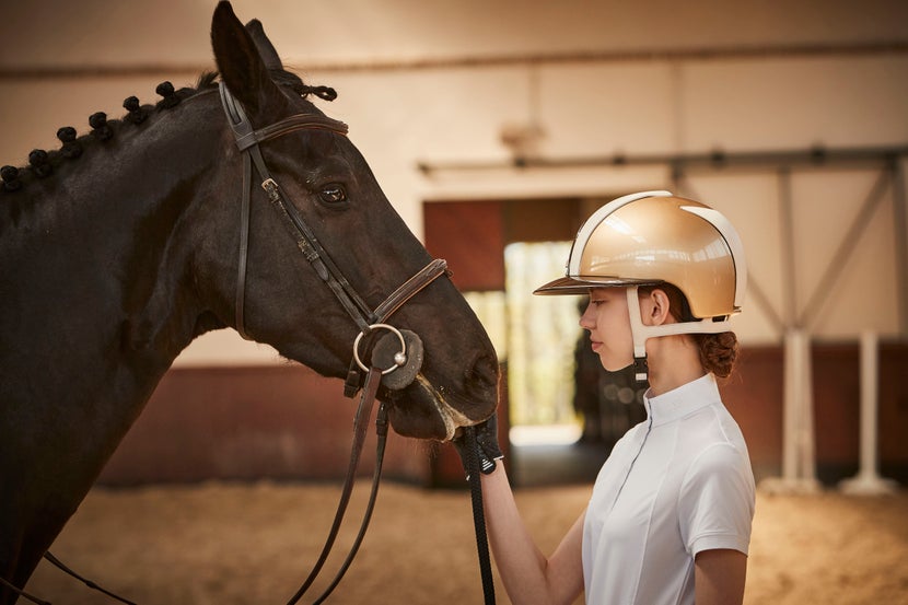 Women wearing KEP helmet petting a bay horse.